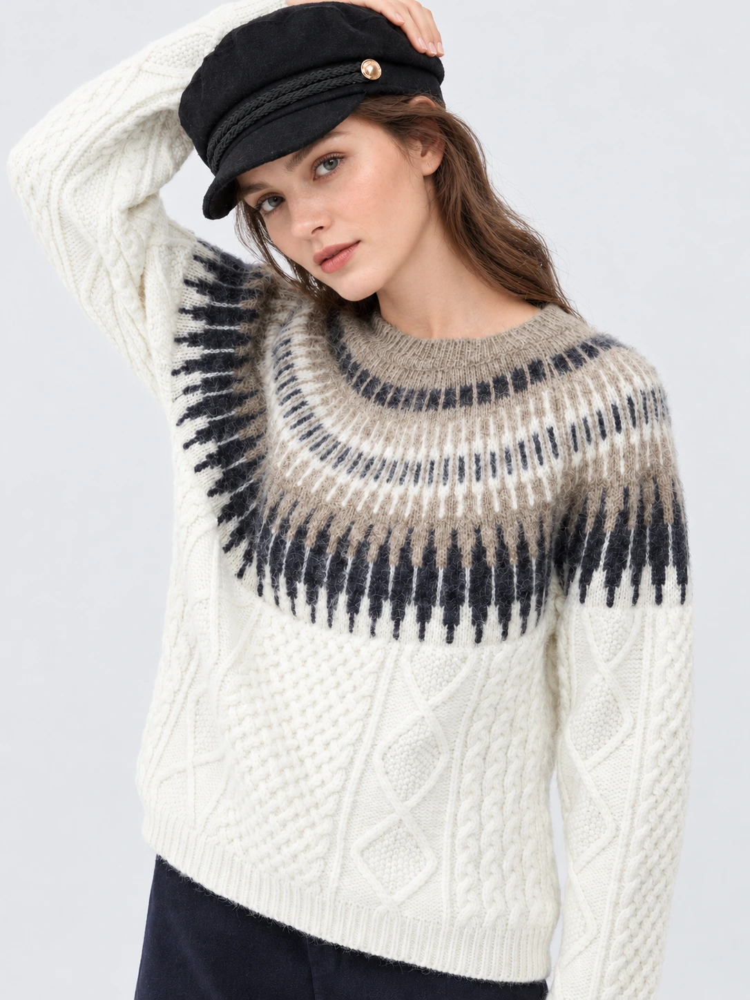Woman wearing a cream cable-knit sweater with a dark patterned yoke and ribbed neckline