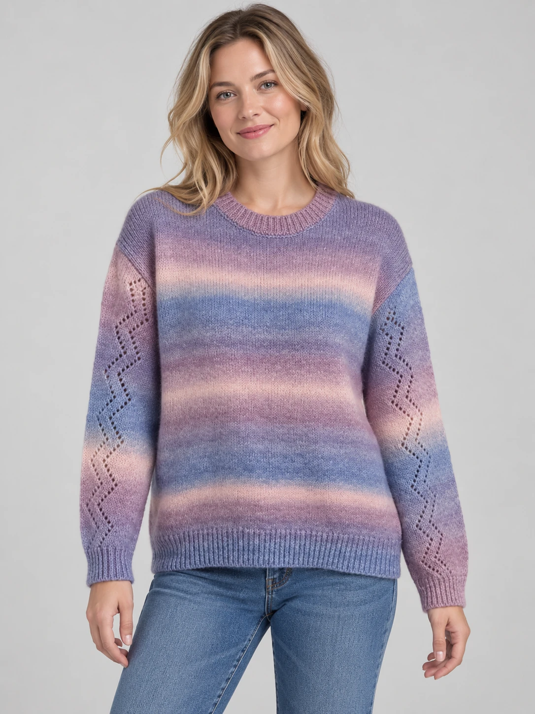 Woman wearing a purple, pink and blue gradient-color crew-neck sweater with diamond-shaped openwork along the long sleeves