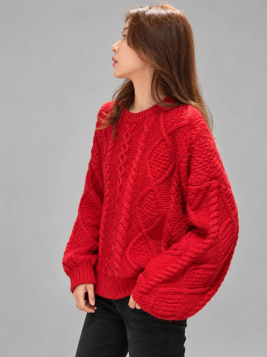 Woman wearing a red long-sleeve crew-neck sweater with prominent cable-knit texture and ribbed edges
